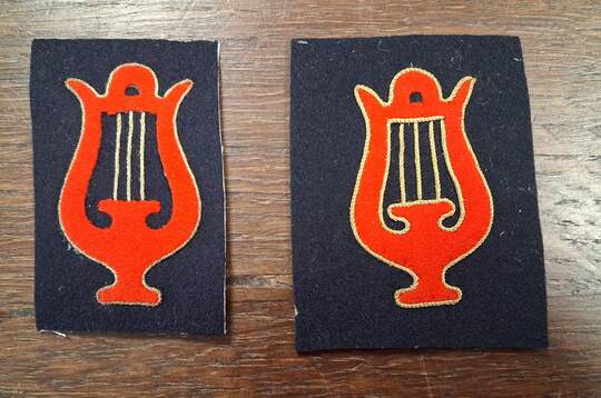 Insigne de spécialité musicien. Lyre découpée rouge, liserée de fil d'or sur draps de laine bleus, cordes dorées . 